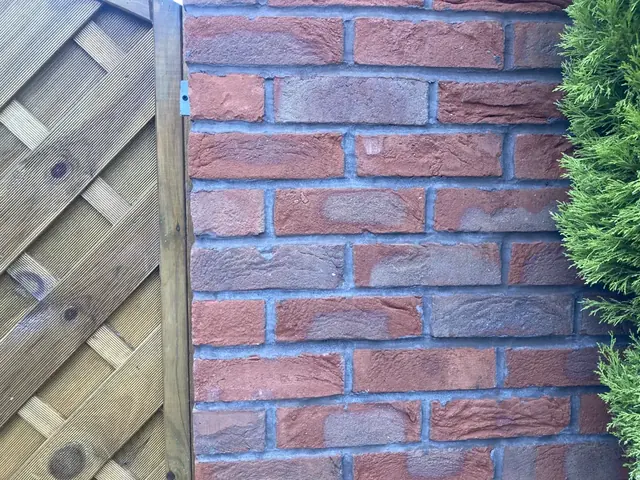 Close-up of new red brickwork and pointing beside a fence panel