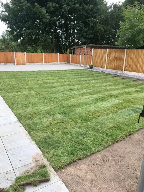 Freshly laid turf lawn beside a pale slab patio and new fencing