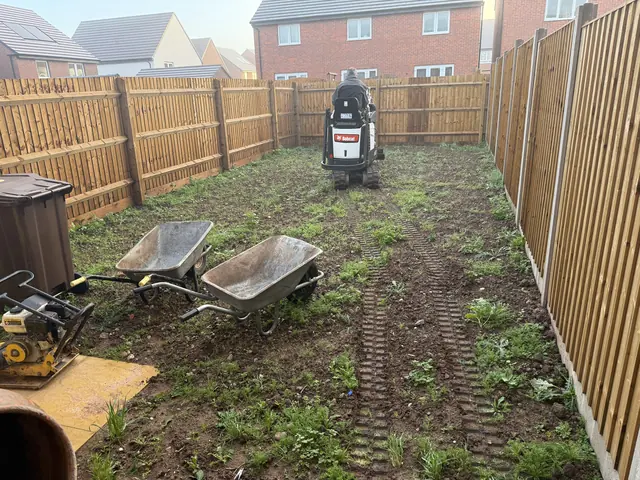 A bare, weedy new-build garden before work started, with Craig on a mini digger